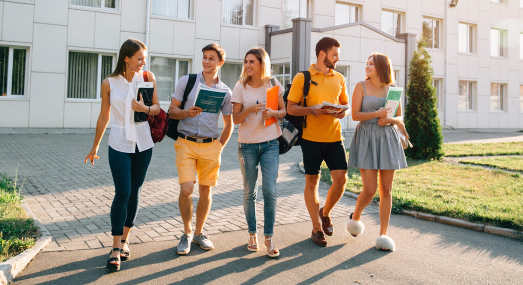 Five friendly students are walking after they passed test outside the college building and discuss the project